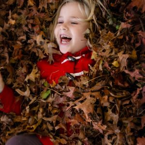 Little girl laying in a pile of fallen raked leaves