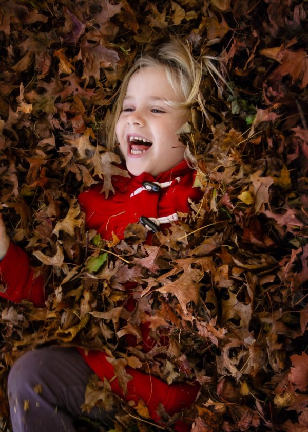 Little girl laying in a pile of fallen raked leaves