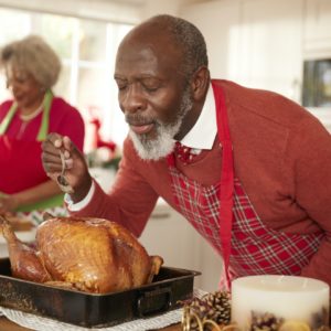 Senior black man basting roast turkey in preparation for Christmas dinner