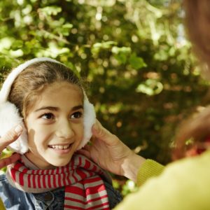 A child wearing warm earmuffs smiling at an adult.