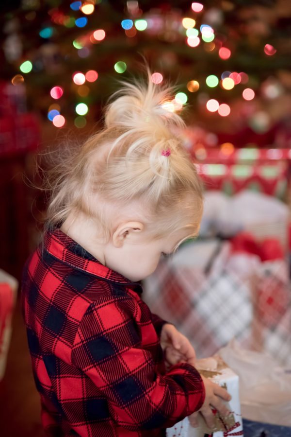 Little girl opening presents on Christmas Day in buffalo plaid pajamas